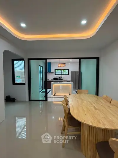 Modern open-plan dining and kitchen area with sleek lighting and wooden furniture.