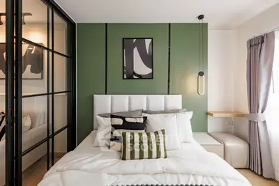 Modern bedroom with stylish decor and green accent wall, featuring a cozy bed and contemporary lighting.