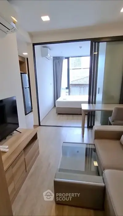 Modern open-plan living room with sleek furniture and glass partition leading to a cozy bedroom.