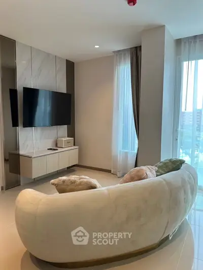 Modern living room with stylish curved sofa and wall-mounted TV, featuring floor-to-ceiling windows for natural light.