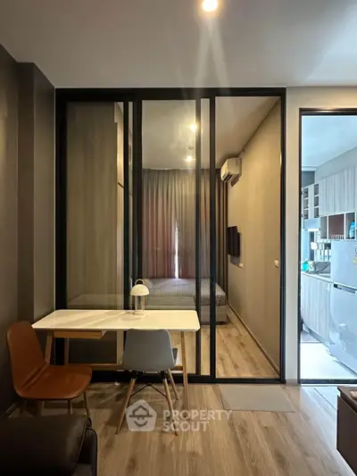 Modern apartment interior with glass partition, cozy dining area, and view into bedroom and kitchen.