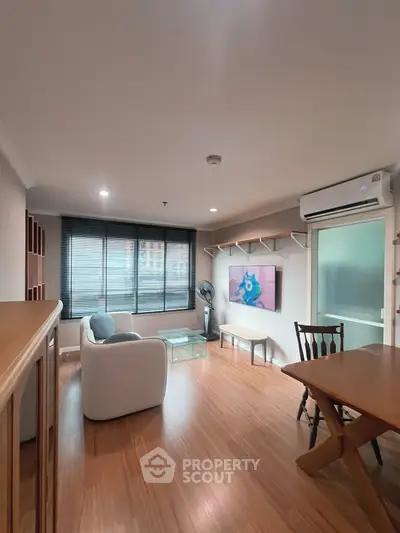 Modern living room with wooden flooring, stylish furniture, and large window offering natural light.