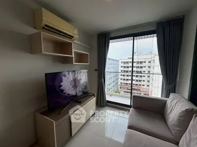 Modern living room with large TV, cozy sofa, and balcony view in urban apartment.