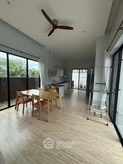 Spacious modern kitchen with open layout and dining area, featuring large windows and stylish ceiling fan.