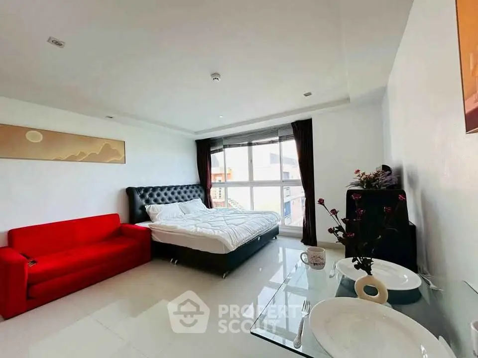 Spacious modern bedroom with red sofa and large window in stylish apartment.