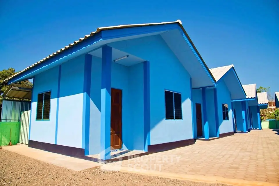 Charming blue single-story house with a spacious paved driveway under a clear blue sky.