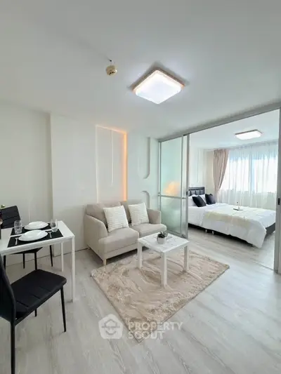 Modern open-plan living room with cozy seating and dining area, leading to a bright bedroom.