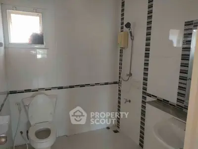 Modern bathroom with sleek white tiles and stylish black accents, featuring a shower and toilet.