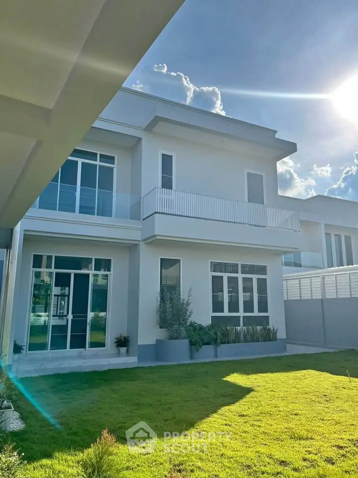 Modern two-story house with large windows and lush green lawn under a bright blue sky.