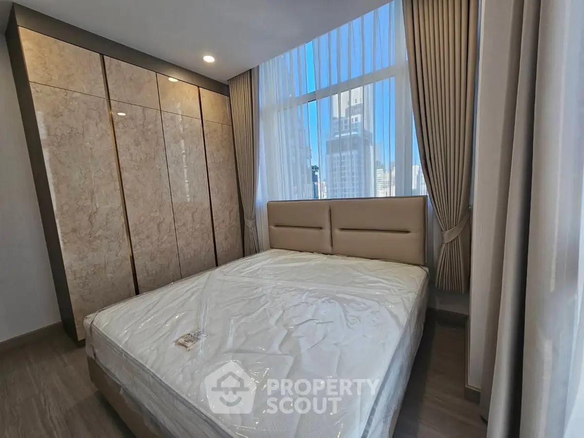 Modern bedroom with large windows and city view, featuring elegant curtains and a spacious wardrobe.