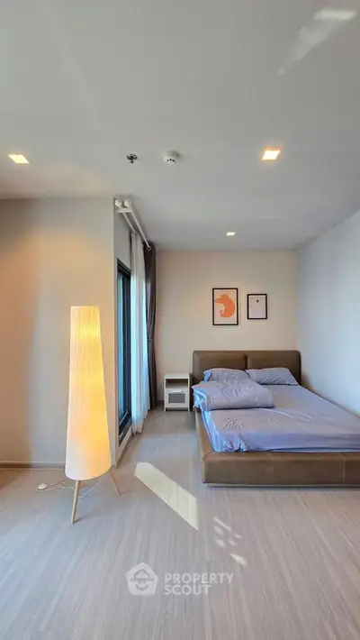 Modern bedroom with stylish decor and natural light, featuring a cozy bed and elegant floor lamp.