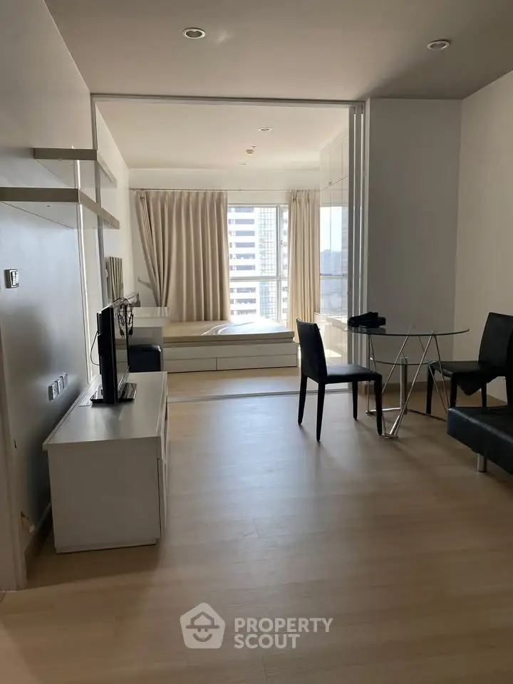 Modern studio apartment with sleek furnishings and large window offering city views.