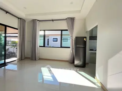 Spacious modern living room with large windows and natural light, featuring sleek tile flooring and a view of the kitchen.