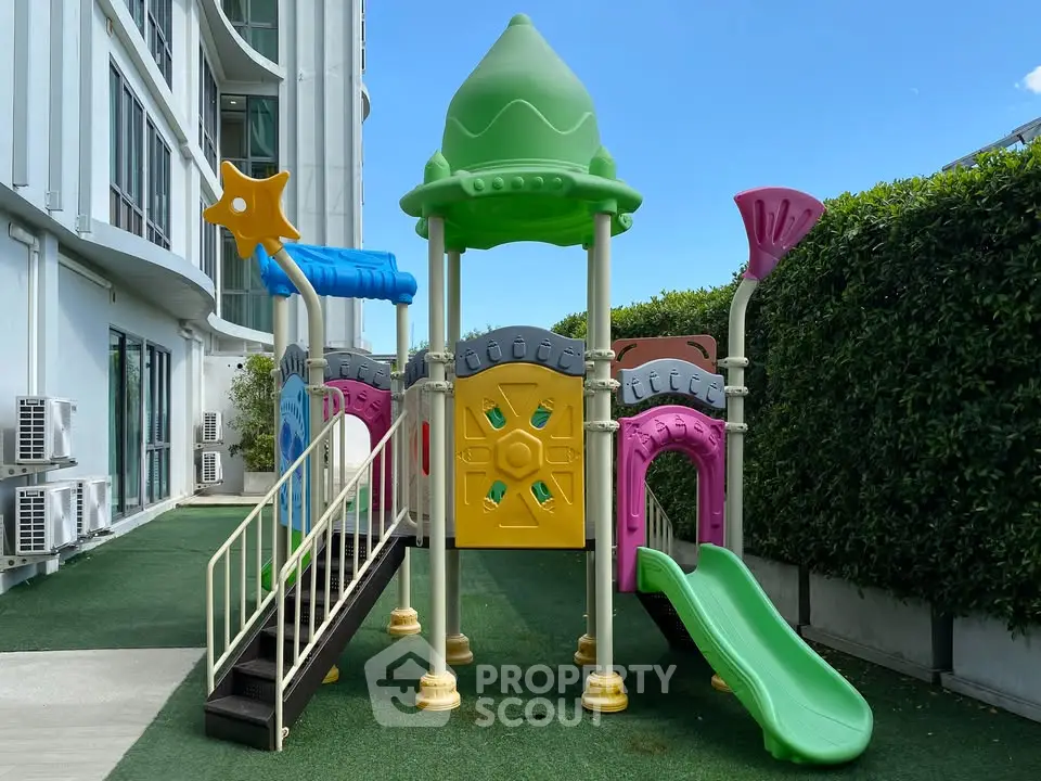 Colorful children's playground in modern residential complex with lush greenery.