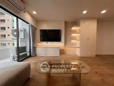 Modern living room with sleek furniture and large TV, featuring a balcony view.