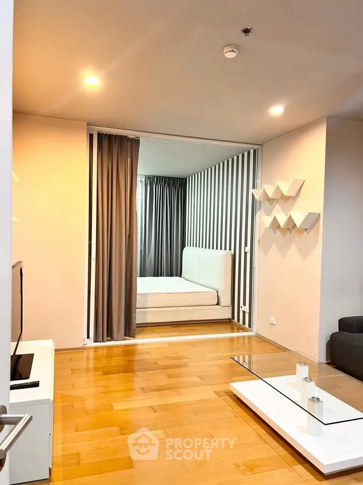 Modern living room with wooden flooring and view into a stylish bedroom with striped accent wall.