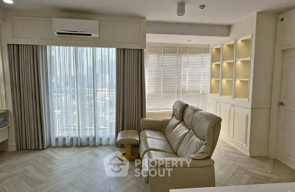 Spacious living room with elegant leather sofa and large windows offering city views.