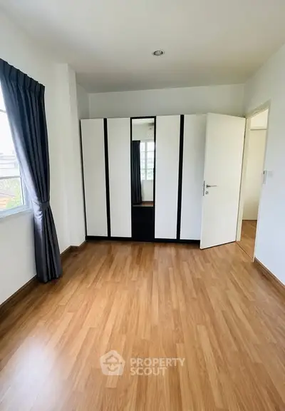 Spacious bedroom with wooden flooring and modern wardrobe, perfect for a cozy living space.