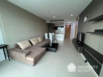 Spacious living area seamlessly connects to a modern kitchen, featuring glossy floor tiles, plush sofa, and sleek entertainment unit, perfect for urban living.