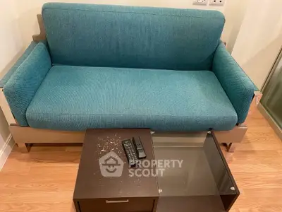 Cozy living room with modern teal sofa and sleek glass-top coffee table on wooden floor.