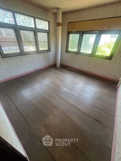 Spacious room with wooden flooring and large windows offering natural light