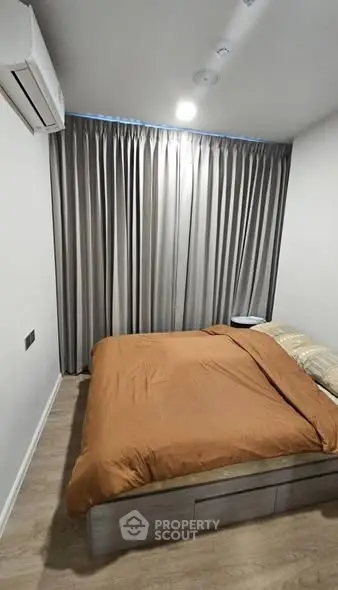 Cozy bedroom with modern decor and wooden flooring, featuring a comfortable bed and elegant curtains.