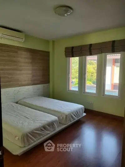 Cozy bedroom with twin beds, wooden flooring, and large windows offering natural light.