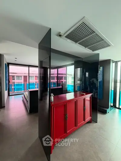 Modern living space with sleek design and vibrant red cabinet, featuring large windows and ample natural light.