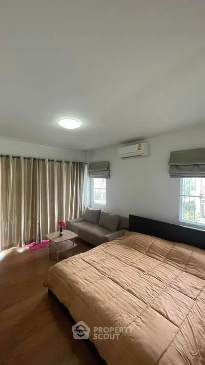 Spacious bedroom with cozy sofa and natural light, perfect for relaxation.