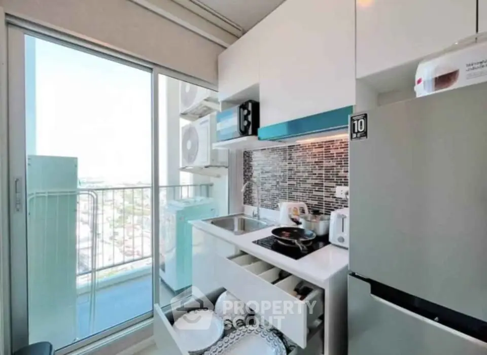 Modern compact kitchen with balcony view, featuring sleek cabinetry and appliances in a high-rise apartment.
