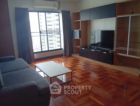 Spacious living room with wooden flooring and large window offering city views.