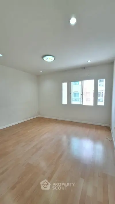 Spacious empty room with wooden flooring and large windows, perfect for customization.