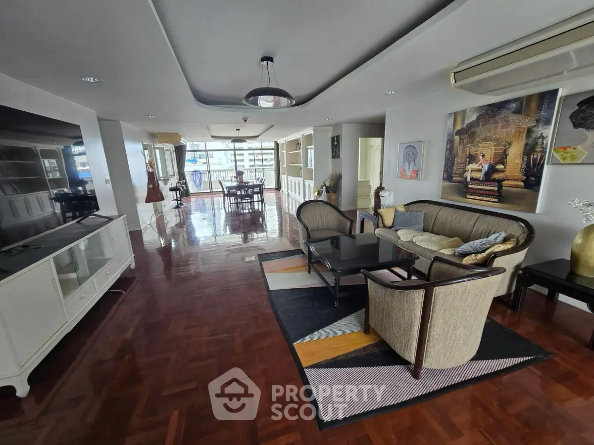 Spacious living room with elegant decor and polished wooden floors, leading to a bright dining area.