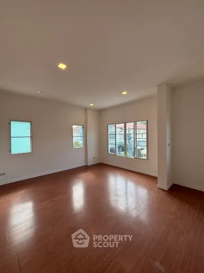 Spacious empty room with wooden flooring and large windows offering natural light.