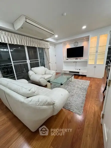 Spacious living room with elegant white sofas, glass coffee table, and modern entertainment center.