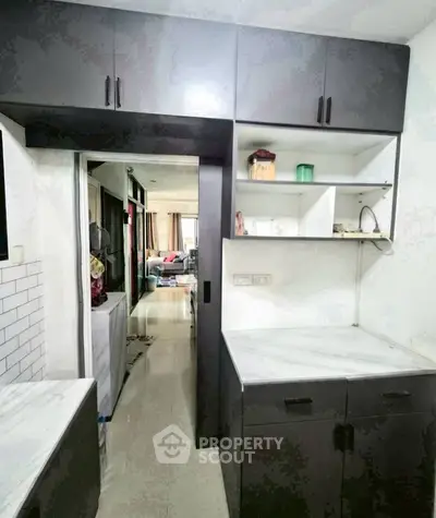 Modern kitchen with sleek black cabinets and white countertops, open layout leading to living area.