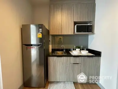 Compact modern kitchen with stainless steel refrigerator, built-in microwave, and sleek cabinetry, perfect for urban living.