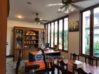 Spacious dining area with ample natural light, elegant wooden furniture, and a view of the lush garden through large windows.