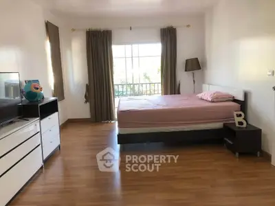 Spacious bedroom with wooden flooring and large window for natural light