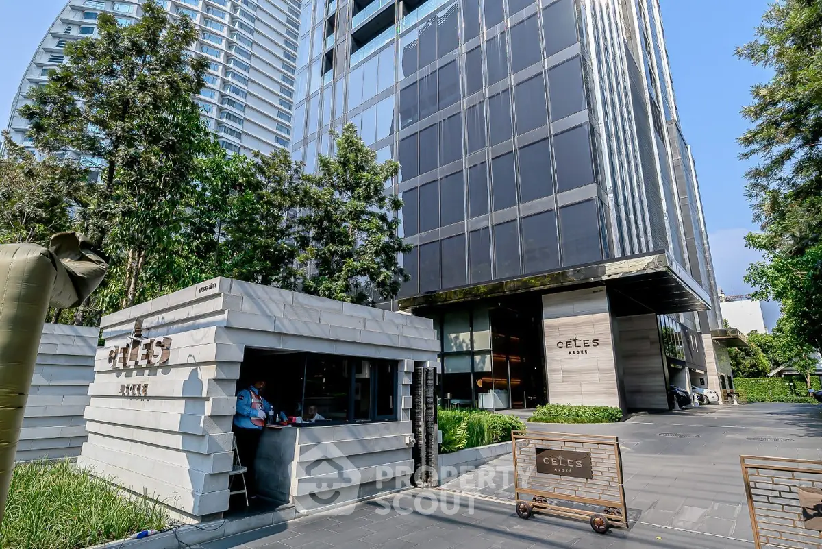 Modern high-rise building with sleek glass facade and lush greenery at entrance.