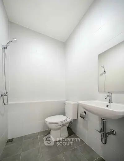 Modern minimalist bathroom with shower, toilet, and sink in a sleek white tile design.