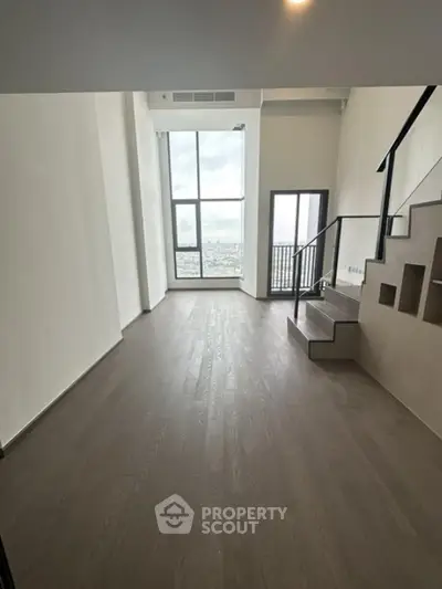 Spacious modern living room with high ceiling and large windows offering stunning city views.