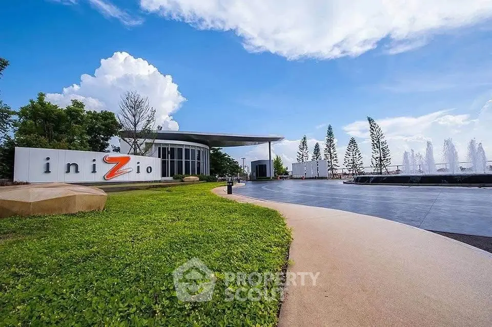Modern building entrance with lush landscaping and water features under a bright blue sky.