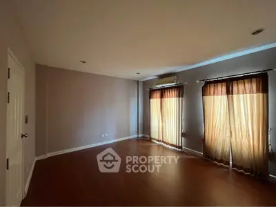 Spacious empty room with wooden flooring and large windows with curtains, perfect for customization.