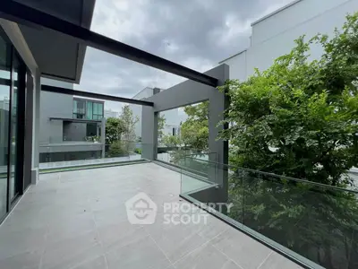 Spacious modern balcony with glass railing and lush greenery view in luxury home.