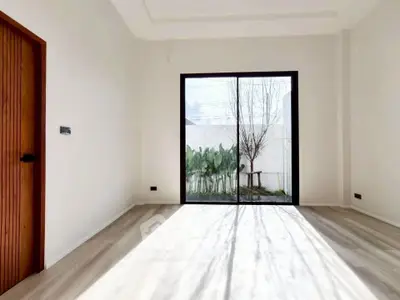 Bright empty room with large glass doors opening to a garden view, featuring light wood flooring and modern design.