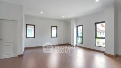 Spacious empty room with hardwood floors and large windows in a modern home.