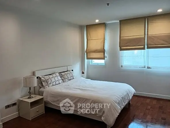 Spacious bedroom with large windows and elegant wooden flooring in modern apartment.