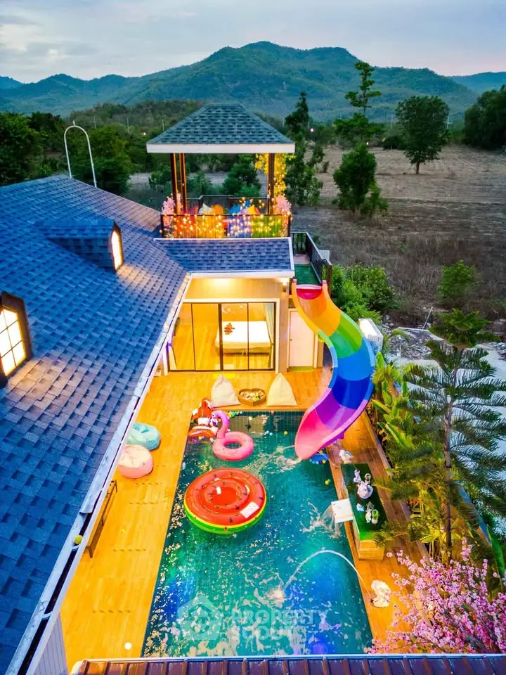 Stunning aerial view of luxury villa with private pool and vibrant slide, nestled in serene natural surroundings.