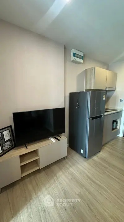 Modern apartment interior with sleek kitchen and living area featuring a flat-screen TV and stainless steel fridge.